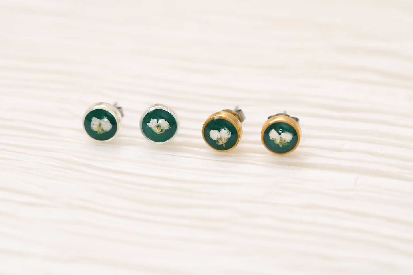two pairs of earrings, a pair of gold and silver dark green circle stud earrings with white dried alyssum flower handmade in clay with resin