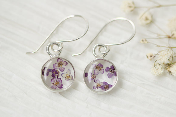 resin earrings in circular silver setting with purple flowers, hanging on handmade sterling silver ear wires