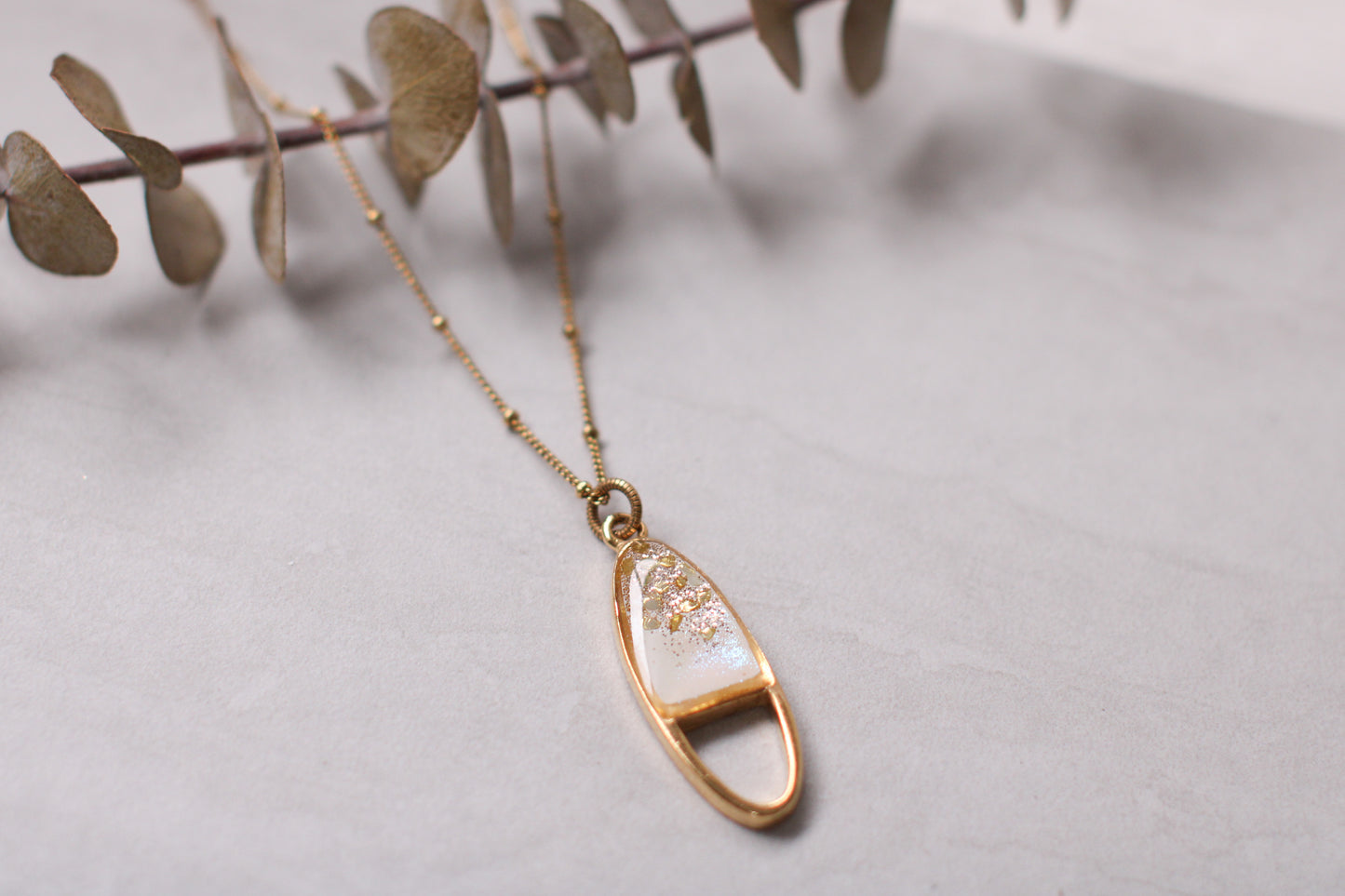 gold sparkly oval necklace on gray tile with plant