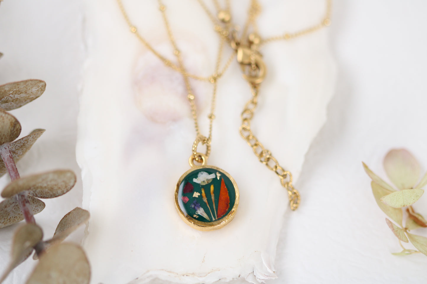 handmade gold dried flower necklace in resin dark green background, circle shaped