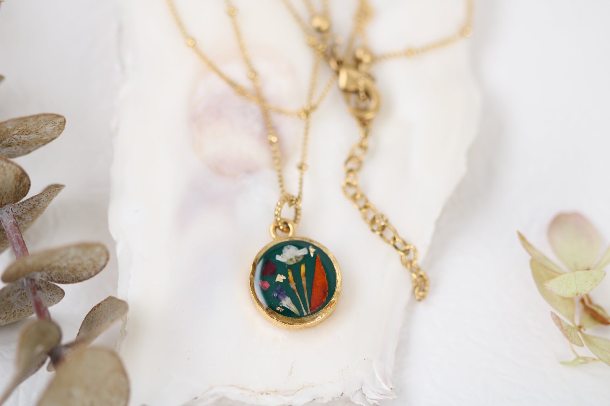 handmade gold dried flower necklace in resin dark green background, circle shaped