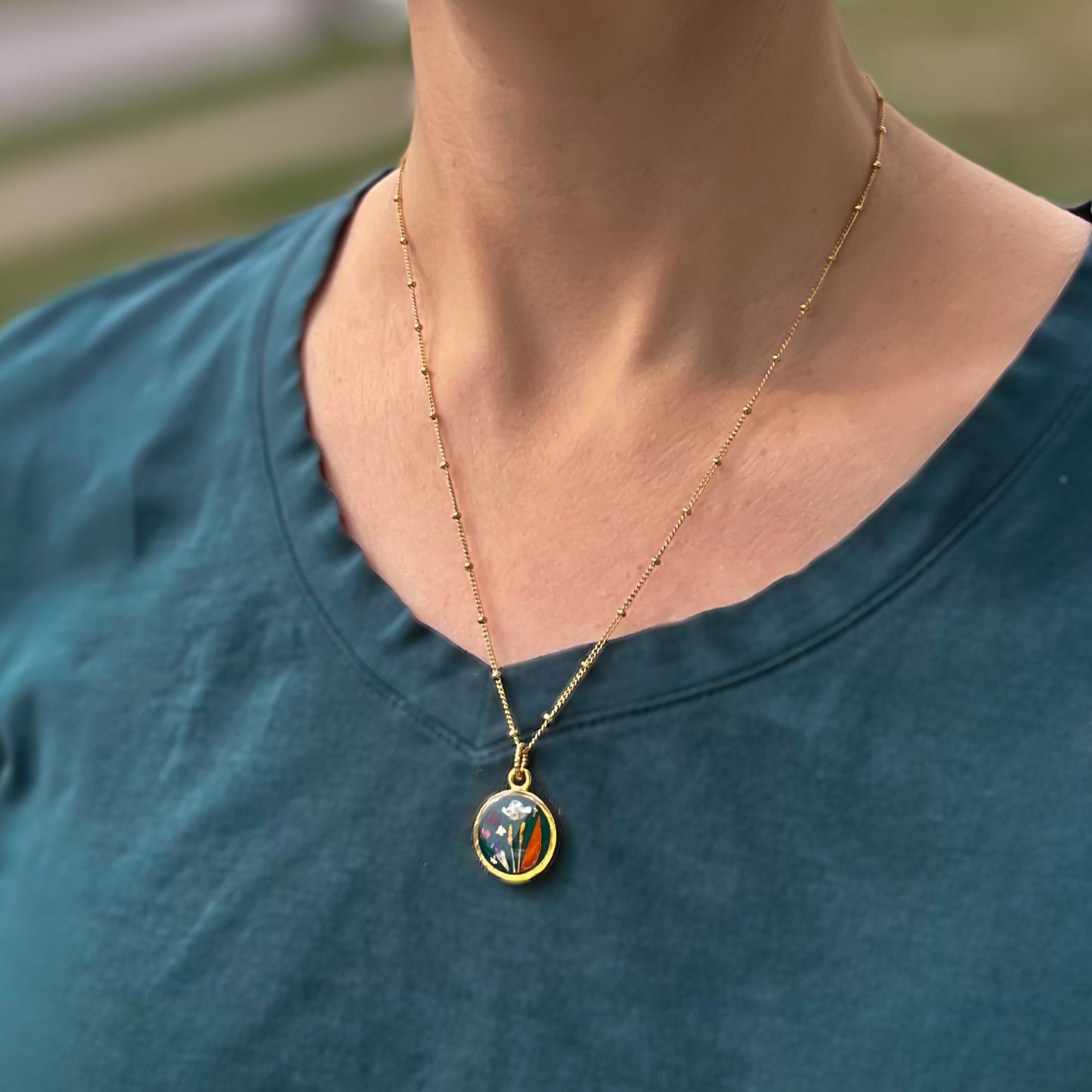 model wearing handmade gold dried flower necklace in resin dark green background, circle shaped