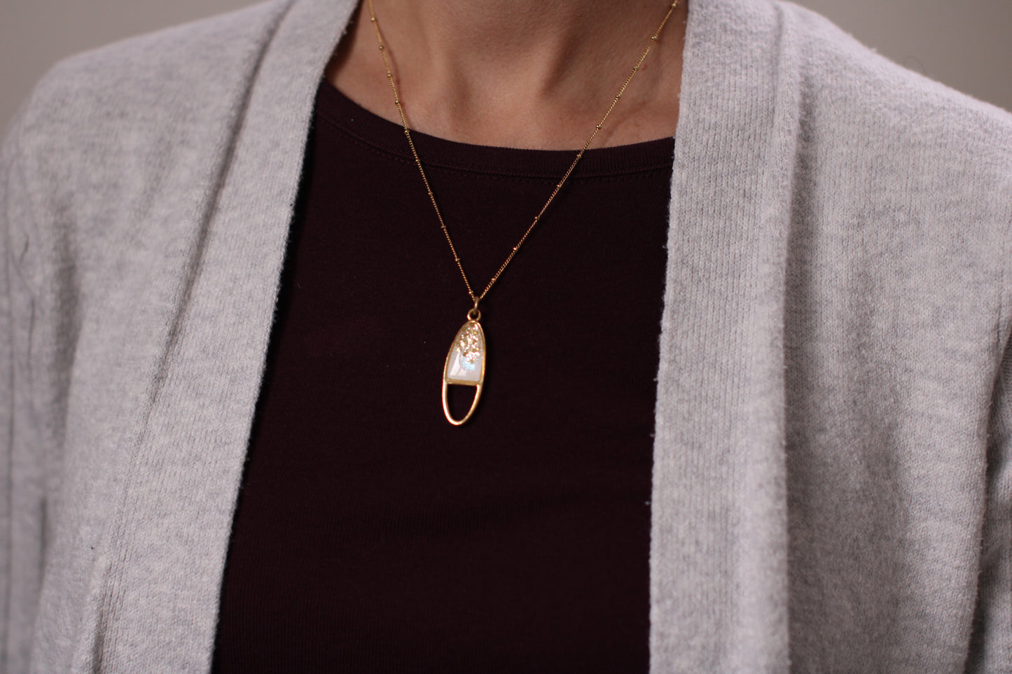 model wearing gold sparkly oval necklace medium sized pendant on 18" chain