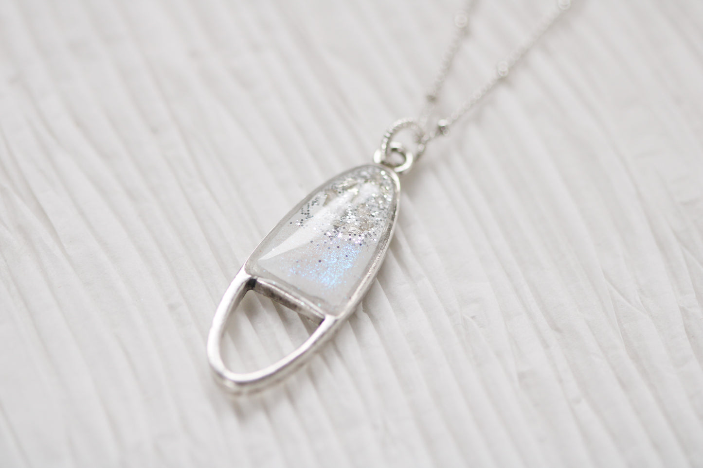 Silver oval shaped necklace with sparkle on white background