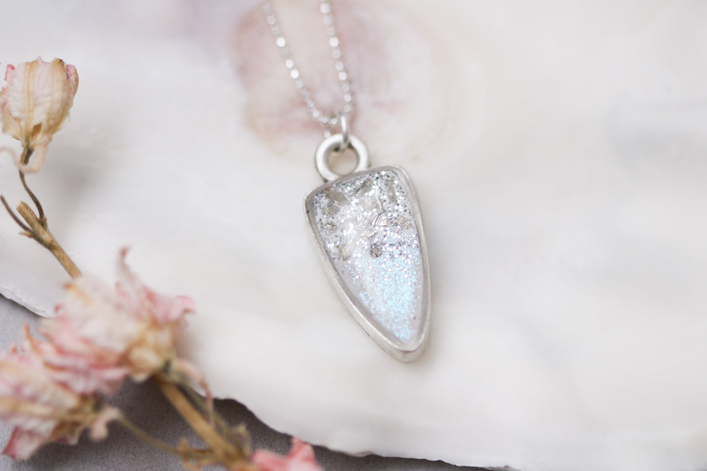 silver sparkly pendant necklace on sterling silver chain, up close photograph on white background with flower