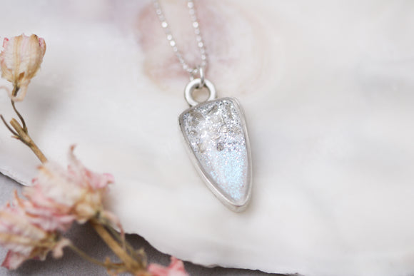 silver sparkly pendant necklace on sterling silver chain, up close photograph on white background with flower