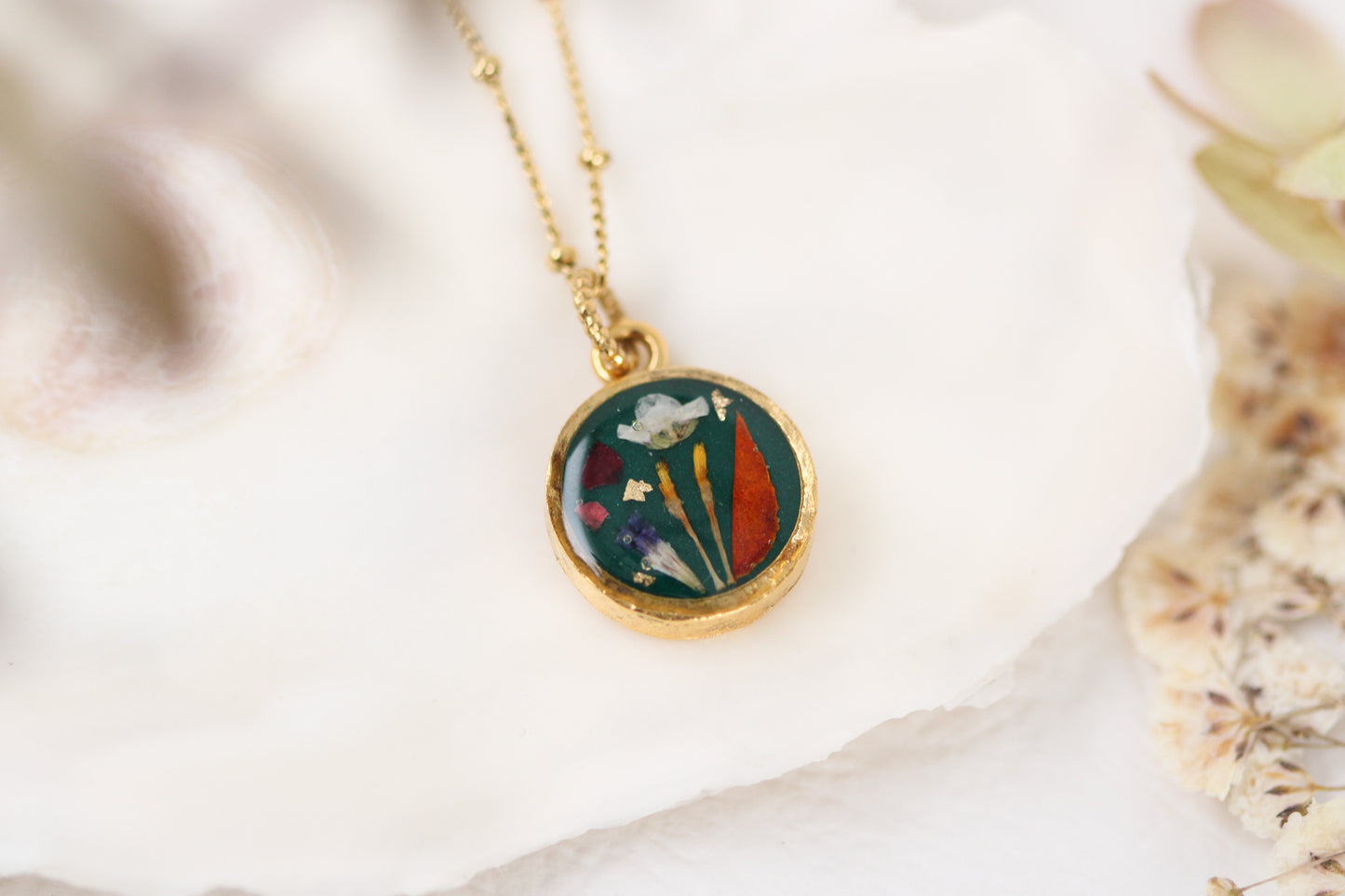 handmade gold dried flower necklace in resin dark green background, circle shaped