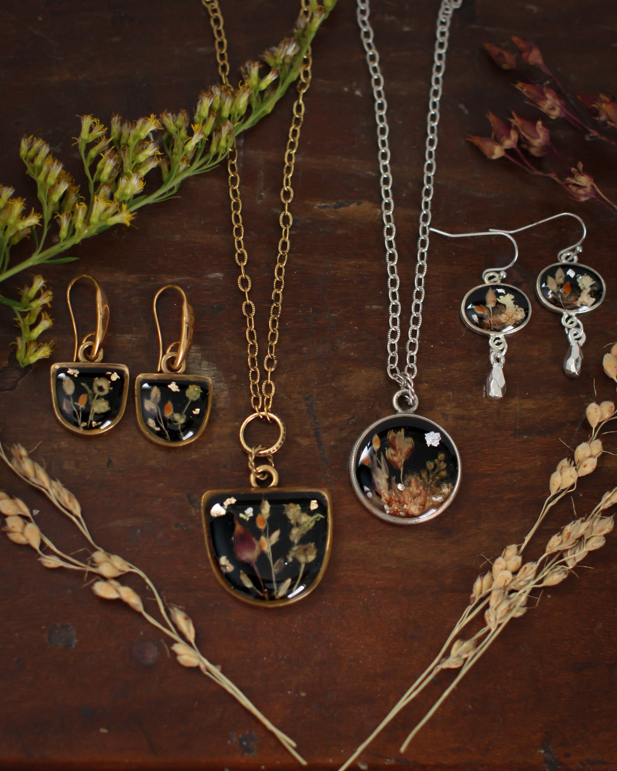 Black handmade jewelry collection made from clay and resin containing real botanical elements such as dried flowers and grain, a fall jewelry collection, 1 gold necklace and earrings, and 1 silver necklace and earrings