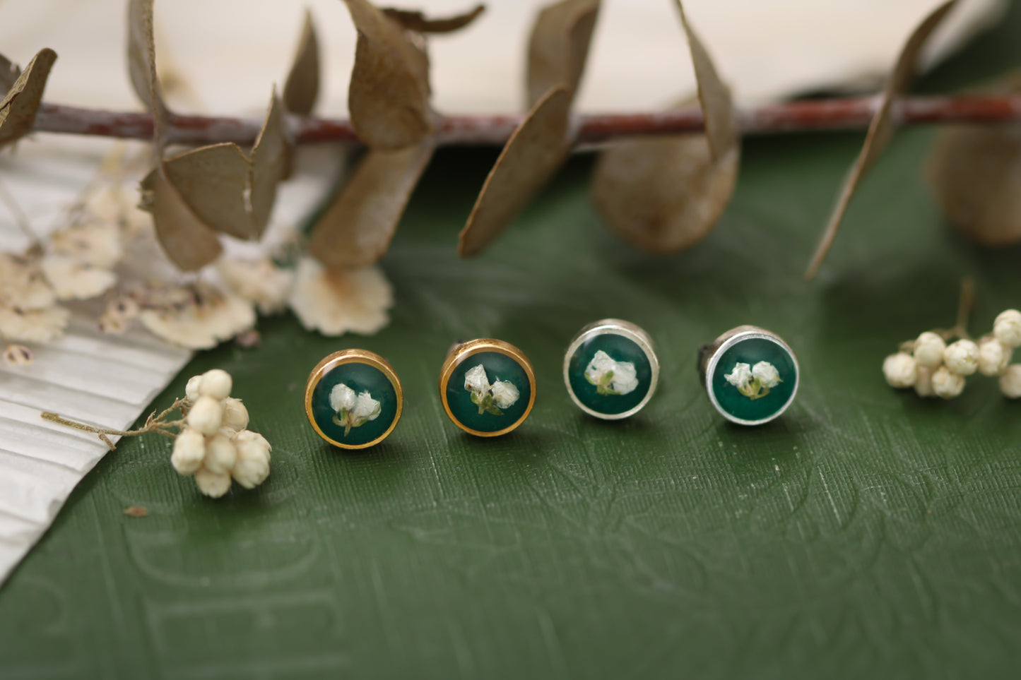 two pairs of earrings, a pair of gold and silver dark green circle stud earrings with white dried alyssum flower handmade in clay with resin