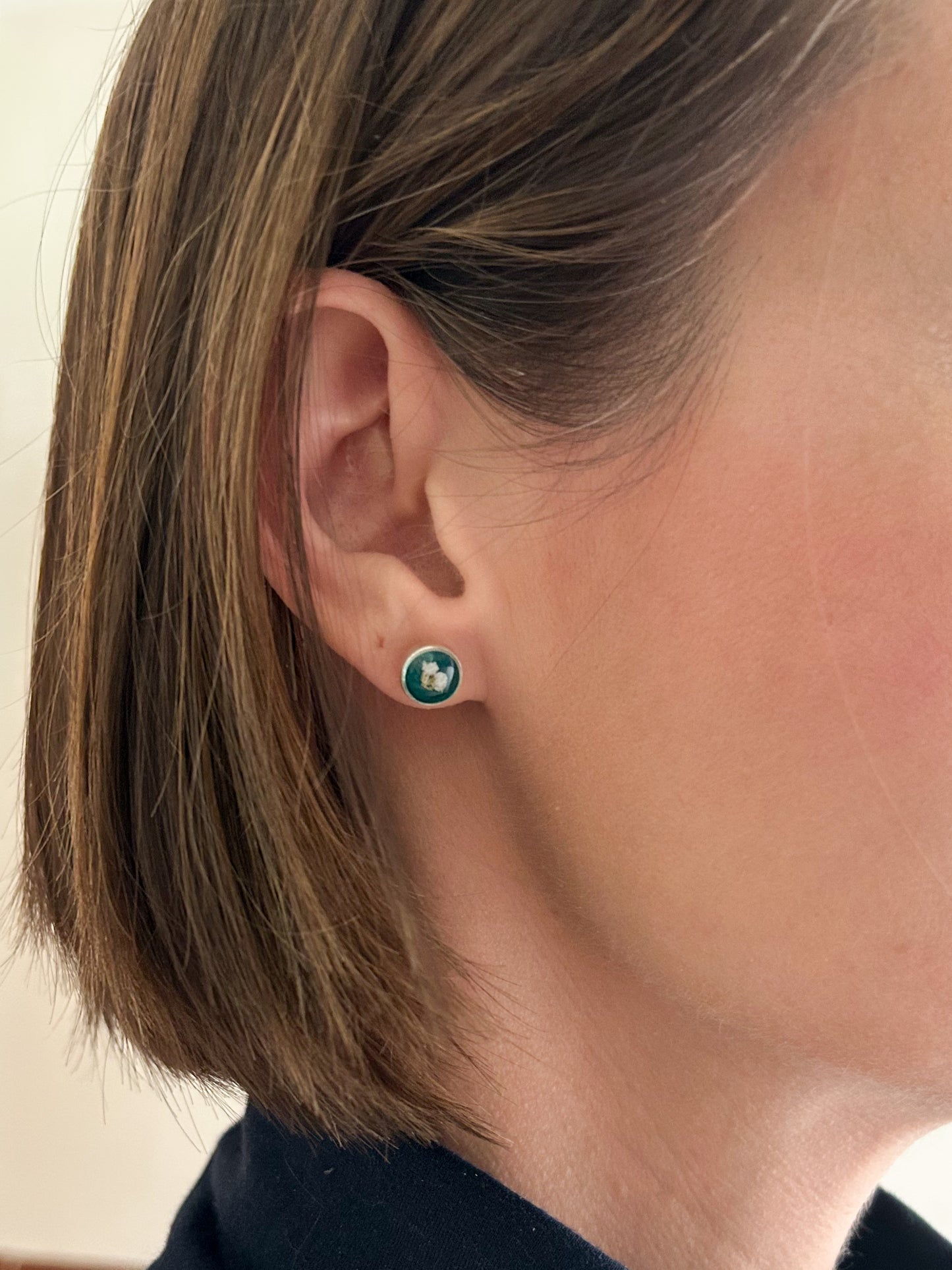model wearing gold and dark green circle stud earrings with white dried alyssum flower handmade in clay with resin