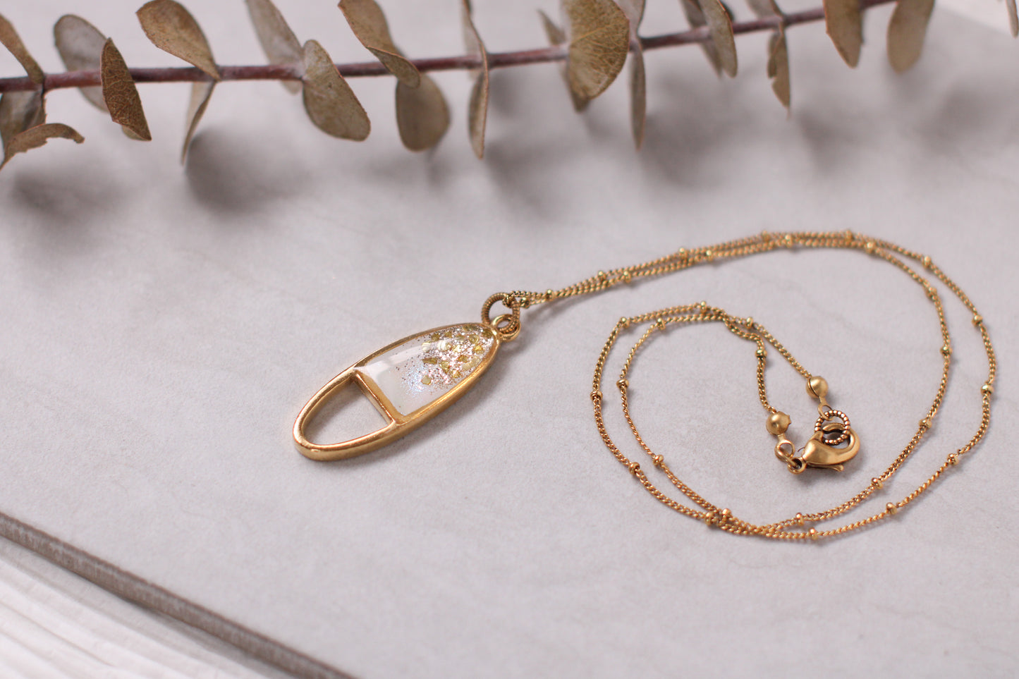 gold sparkly oval necklace on gray tile with plant